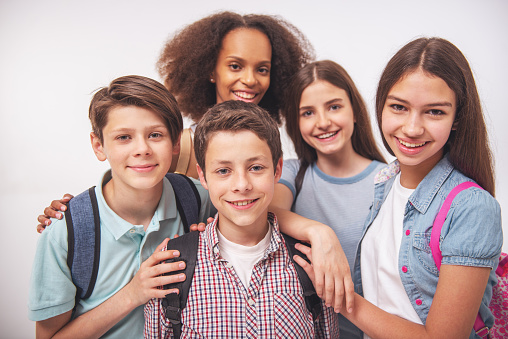 Group of teenage boys and girls with school backpacks is looking at camera and smiling, isolated on white