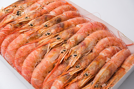 Close up image depicting a pile of frozen prawns defrosting in a metal sieve.