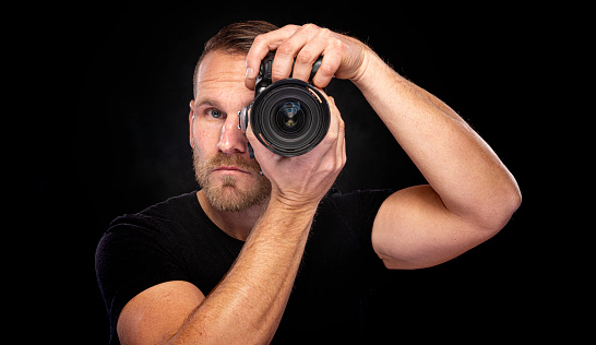 A man with a beard takes pictures with a camera on a dark background.