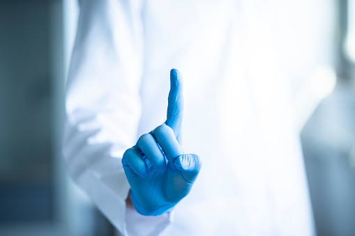 A close-up shot of a person wearing blue gloves, pointing with their index finger