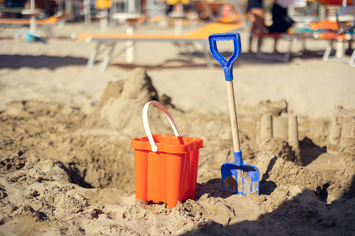 Children's bucket and shovel, castle of sand on the sand beach on a sunny day. Toys for kid play on the sea side. Travel on the beach concept. Vacation concept. Children games in the sand