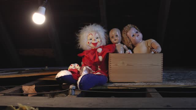 Lightbulb Swinging Over Box of Creepy Dolls in Attic