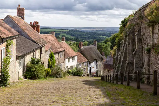 Old English houses with red roof tiles and thatched roofs and with green hills in the background (Golden hill) in the picturesque village of Shaftesbury, Dorset, England.