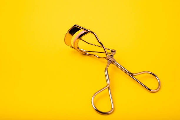 istock Golden eyelash curler on a yellow background close-up. 1489539955