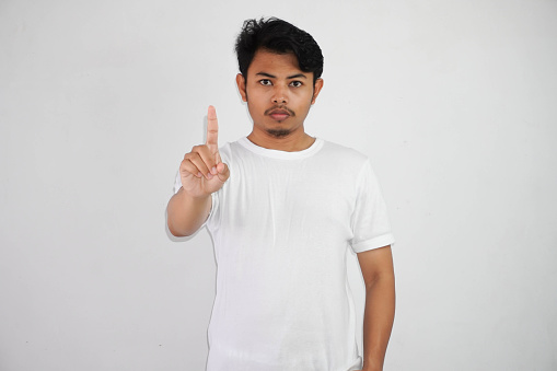 serious young Asian man showing stop gesture, demonstrating denial sign wearing white t shirt isolated on white background
