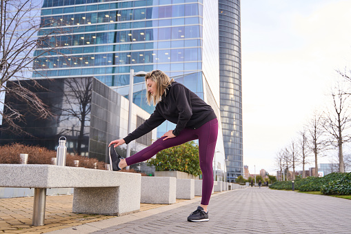 young woman in sportswear stretching her legs before training, getting ready to run.