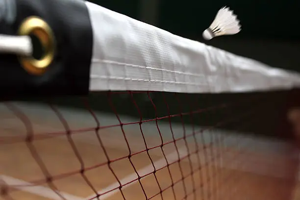 Photo of shuttle badminton net up close and a fast moving shuttlecock above the net in a indoor badminton court