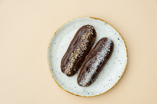 Eclairs in round plate flat lay composition on beige background.