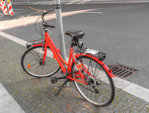 A red bicycle is parked at a lamppost on a city street.