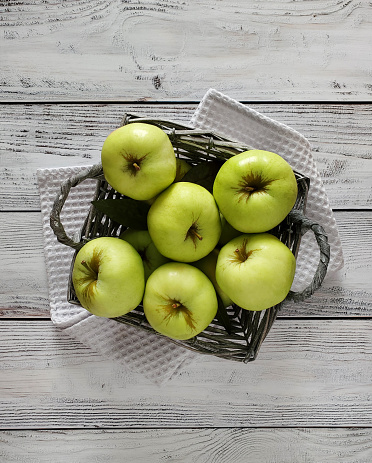 Basket of green apples on light wooden background, top view.