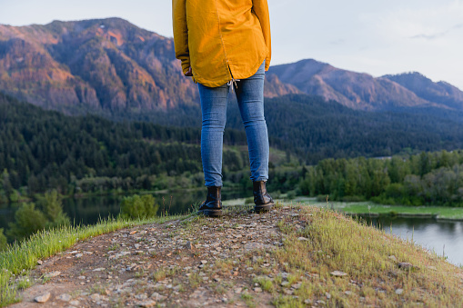 A young woman standing in nature wearing a yellow jacket and blue jeans for a pop of color. She is hiking/exploring the Columbia river gorge scenic area of Oregon.