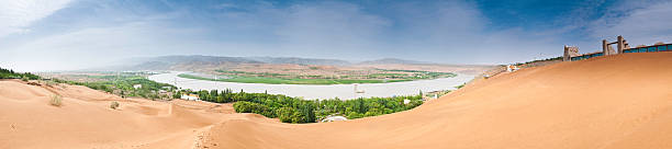 Panoramic vista over the huge sand dunes along the banks of the Yellow River (Huang He) and the Shapotou Desert Experimental Research Station and theme park, a popular local tourist oasis destination in the Ningxia Province of China. ProPhoto RGB profile for maximum color fidelity and gamut.