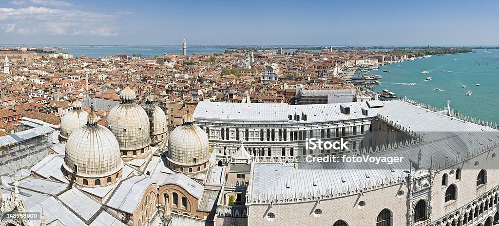 Venice Basilica Doges Palace lagoon vista Aerial view over the Byzantine domes of the Basilica di San Marco and the ornate arches and arcades of the Doge's Palace overlooking the blue waters of the Venetian lagoon and Lido to the leafy park around the Arsenale, the terracotta rooftops and campaniles of the Castello district and the distant islands of San Michele and Murano from the famous Campanile in St. Mark's Square. ProPhoto RGB color profile. Aerial View Stock Photo