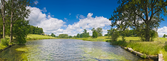 Panoramic blue summer skies over verdant valley vista with green meadows, reeds, trees and pasture on the banks of this idyllic rural river. ProPhoto RGB profile for maximum color fidelity and gamut.