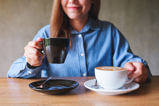 Closeup image of a young woman holding and drinking two cups of hot coffee