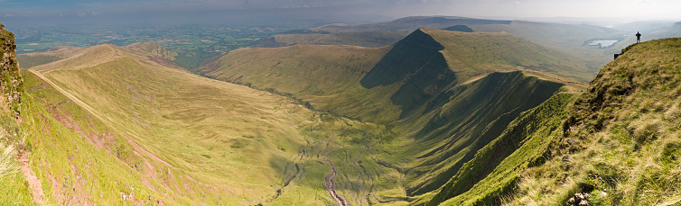 Walker on mountain top overlooking a dramatic wilderness escarpment, green valleys and sweeping panoramic views. ProPhoto RGB profile for maximum color fidelity and gamut.