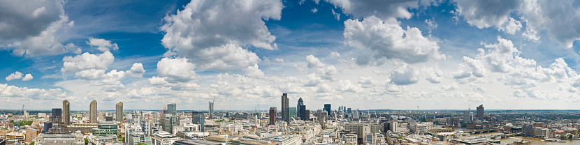 Big skies and white fluffy clouds over a sweeping panoramic vista across the skyscrapers, streets and landmarks of the City of London, the UK's financial and business centre, from the Barbican, past the iconic towers around the Bank of England and the skyscrapers of Canary Wharf and Docklands, to the banks of the Thames, Tower Bridge, City Hall, Shakespear's Globe Theatre and the distant aerials of Crystal Palace. ProPhoto RGB profile for maximum color fidelity and gamut.