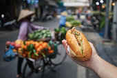Hand holding Banh Mi sandwich on street in Hanoi