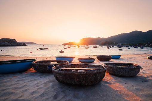 Basket boats on sand beach in bay against sea at beautiful sunset. Fishing village on Cham Islands in Vietnam.