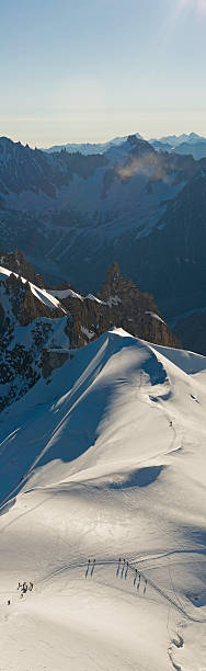 Alpinists glacier summit dawn Early moring sunlight casting long shadows from the mountaineers high on a snowy col surrounded by dramatic jagged pinnacles, glaciers and cornices on the Mont Blanc Massif, France. ProPhoto RGB profile for maximum color fidelity and gamut. winter sunrise mountain snow stock pictures, royalty-free photos & images