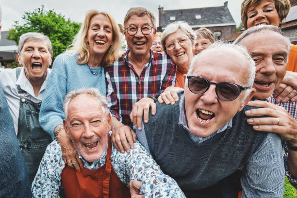 Joyful Seniors Taking a Group Selfie A lively group of over-65 friends gathered at a countryside house, laughing and shouting together as they take a joyful group selfie. baby boomer stock pictures, royalty-free photos & images