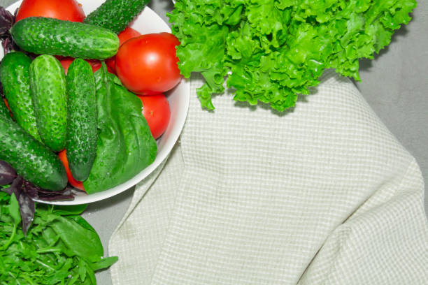 Spinach, greens, cucumbers, tomatoes, basil collected at their dacha lie in a white bowl, in a gray kitchen for cooking delicious and fragrant dishes...