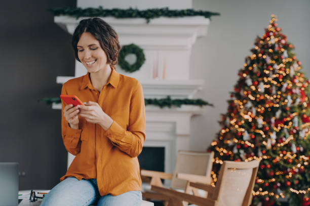 istock Joyful european woman using cellphone while sitting home office with Christmas tree on background 1489649639