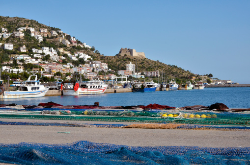 Fishing port and town of Roses, or Rosas, with fishing nets and the Castell de la Trinitat in the background. Roses is a commune on the Costa Brava at northeastern Catalonia in Spain.