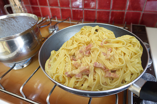 Tagliatelle pasta with carbonara sauce and bacon being cooked