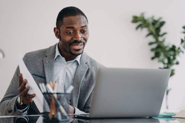 istock Happy man has video call on laptop and pointing to data papers. Remote african executive. 1489656139