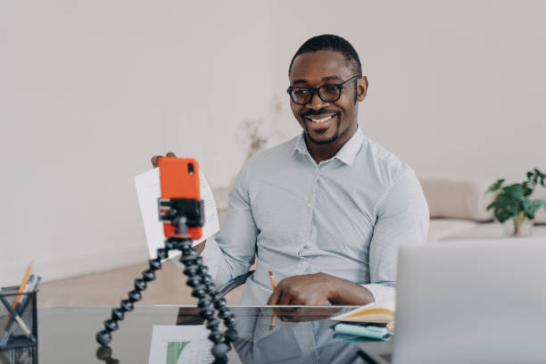 istock Afro freelancer has online brainstorm on smartphone. Happy man shows paperwork with data. 1489656151