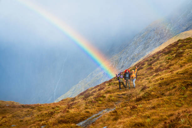 istock Hikers on mountain trail with rainbow sky backdrop. 1489666870