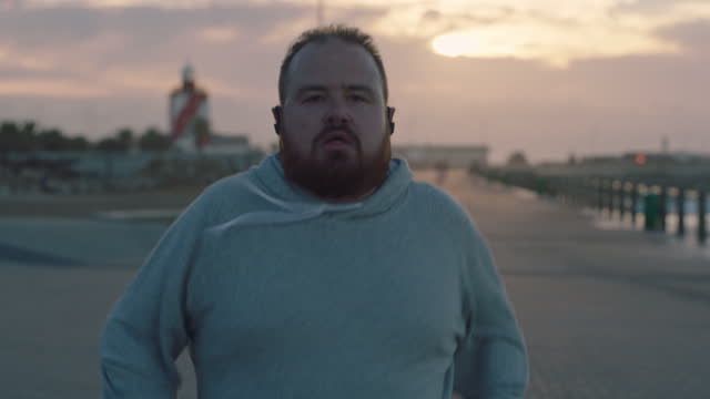 overweight man running intense workout challenge obese caucasian male exercising on seaside at sunset close up