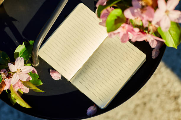 Open notebook and flowers and on the small black table on terrace at home in a sunny day, hardlight, outdoor workspace, summer relaxation, notes, ideas, planning
