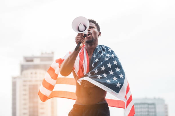 hombre afroamericano con la bandera de estados unidos gritando en un megáfono en protesta, black lives metter - black civil rights fotografías e imágenes de stock