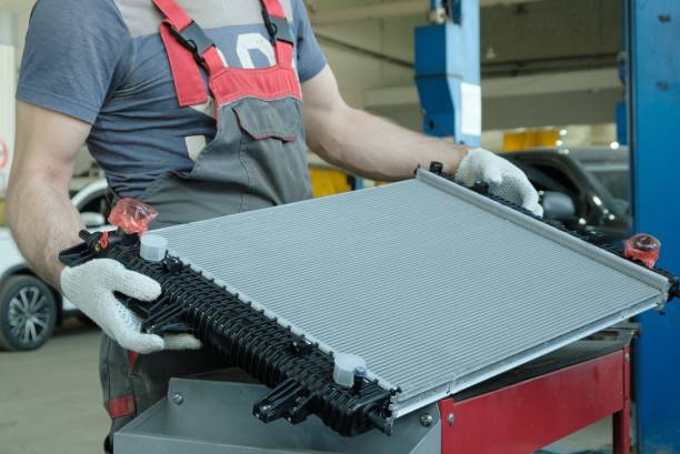 An auto mechanic holds a new engine cooling radiator in his hands.