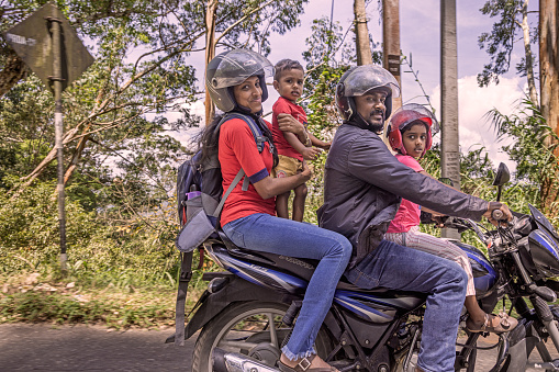 Kandy, Central Province, Sri Lanka - February 25th 2023:  Happy family with two kids on a motorcycle seen from a passing car