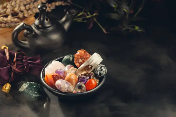 Bunch of Colorful Crystals and Rough Mineral Stones in the Black Bowl Shrouded in a Mystical Mist. Crystal Healing Concept. Copy Space for Text