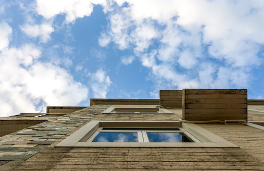 Looking up the side of a house up to the blue sky and white clouds above that are reflected in the window
