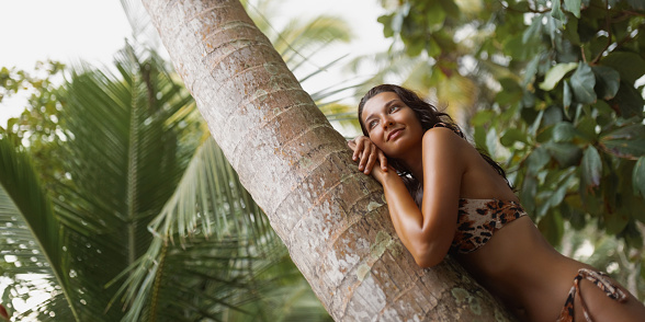 A young adult woman wearing a fashionable leopard print bikini blissfully laying in the tropical rainforest. She appears carefree and happy as she enjoys her dreamy weekend getaway.