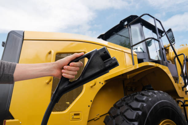 Hand with electric plug on a background of electric tractor Hand with electric vehicles charging plug on a background of electric tractor construction vehicle stock pictures, royalty-free photos & images
