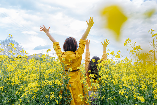 back view of mother and daughter in yellow clothes standing with arms up in the field with yellow flowers