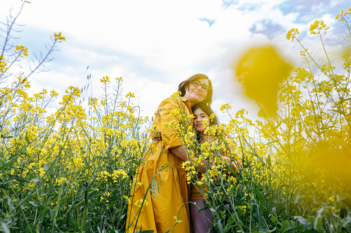 mother in yellow dress holding a child with long dark hair in arms in a field with yellow flowers