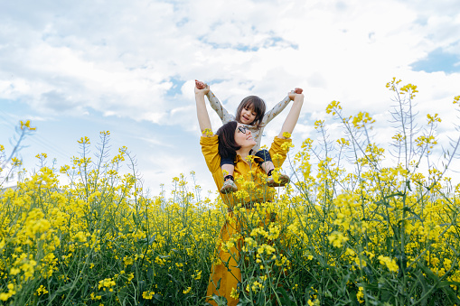 smiling child sitting on mother in the field with yellow flowers