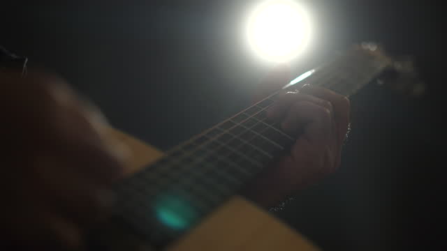 Close-up guitar of Attractive singer man singing music and playing guitar on stage with spotlight strike through the darkness at concert event. Musician performing live with light and smoke at hall.