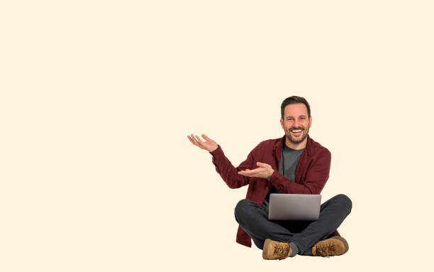 istock Cheerful young male professional showing copy space for marketing while working over laptop on background. Businessman happily gesturing and advertising while sitting with legs crossed 1489752761