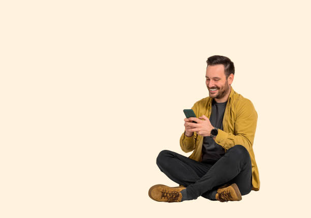 istock Smiling male entrepreneur texting over mobile phone while sitting with crossed legs against background. Happy young executive dressed in business casuals sending message to client over cellphone 1489752771