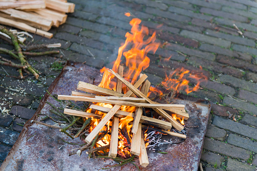 Step 4 in making a fire with very limited means: adding some small and dry sticks to the initial fire created with tinder, wood shavings and twigs in order to grow the fire.