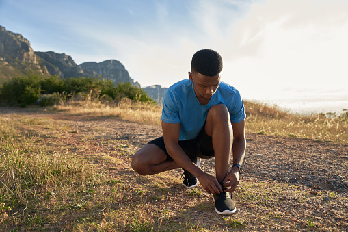 Black young Adult male focussed while tying his shoelaces, about to start his morning mountain run. High Quality Photo