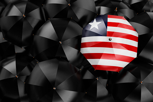 Umbrella with Liberian flag among black umbrellas, top view. 3D rendering